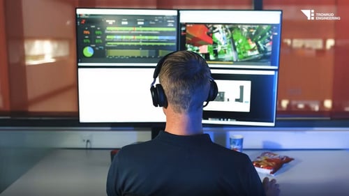 Operator wearing headphones monitors Tronrud iNSIGHT dashboards and live line video on dual screens from a workstation overlooking the production area.