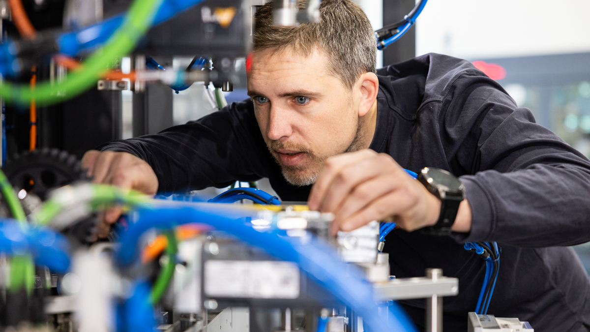 Engineer adjusting pneumatic hoses and components on an industrial packaging machine during assembly in a workshop.