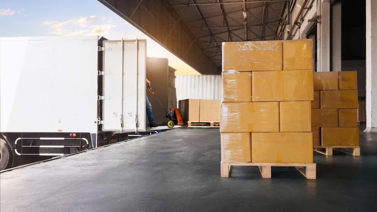 Pallet of shrink-wrapped cardboard boxes at a warehouse loading dock beside a truck.
