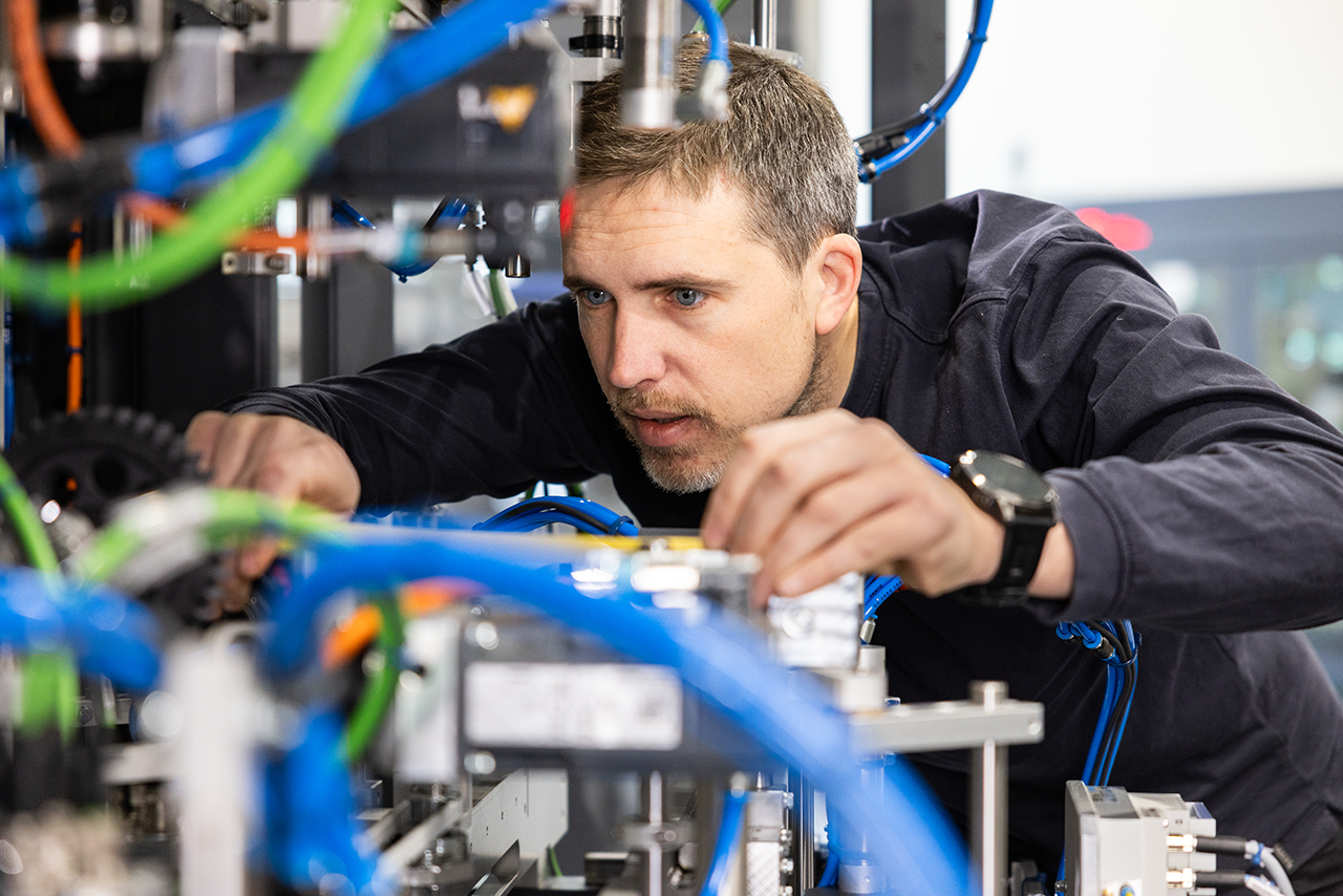 Engineer adjusting pneumatic hoses and components on an industrial packaging machine during assembly in a workshop.